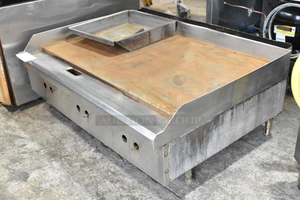 Stainless steel commercial countertop gas flat top griddle. Features durable construction with temperature controls. Some surface wear visible.