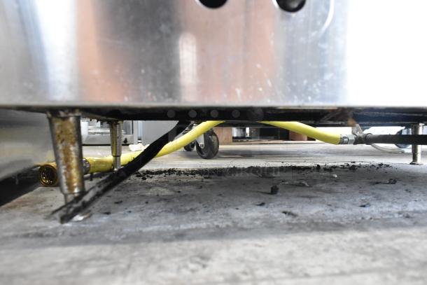 Stainless steel commercial countertop gas griddle underside showing yellow gas line, wheels, and surface wear.