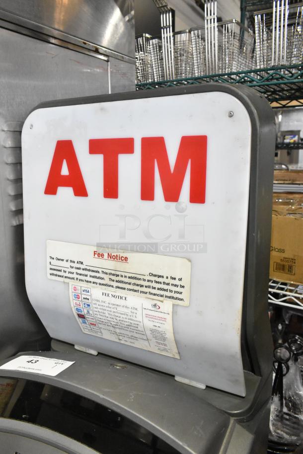 Hyosung Metal Floor Style ATM, large "ATM" sign, fee notice visible, industrial setting, used condition.