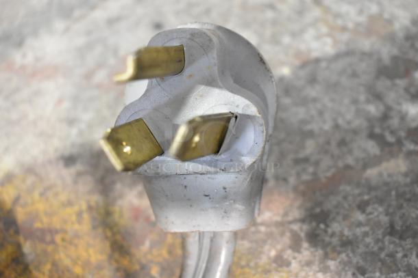 Close-up of a three-prong power plug for the Bunn DUAL SH coffee machine, showing metal prongs and a white plug housing.