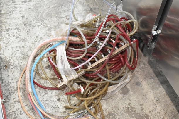 A pile of assorted colored hoses and cables on the ground next to a metal commercial appliance.