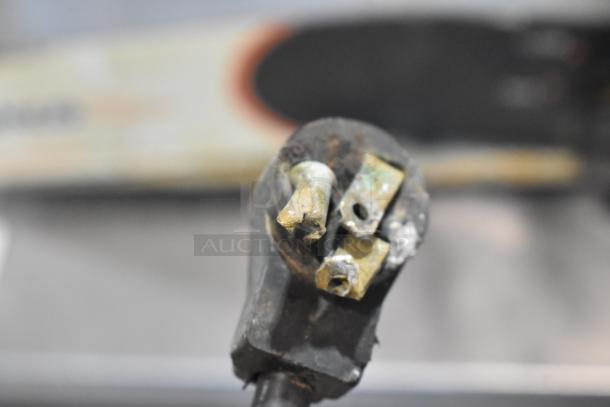 Corroded electrical plug with damaged prongs and wear, indicating need for repair or replacement. Background blurred.