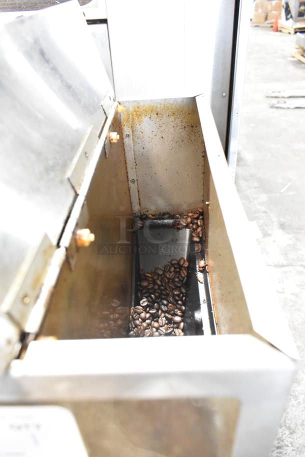Metal commercial countertop coffee bean grinder, 120 volts, 1 phase. Slightly worn interior with some visible coffee beans.