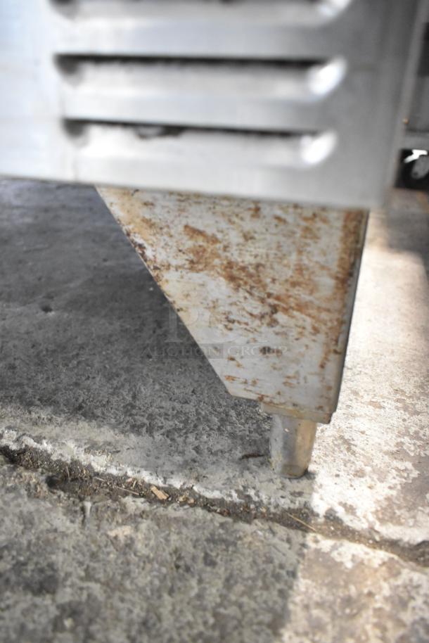 Close-up of a rusted metal corner and leg, possibly of industrial kitchen equipment, on a concrete floor.