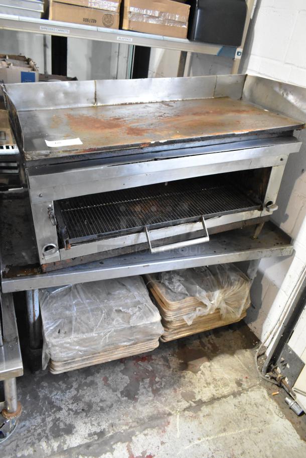 Stainless steel commercial gas griddle with cheese melter on stand, shows signs of wear, includes storage below.