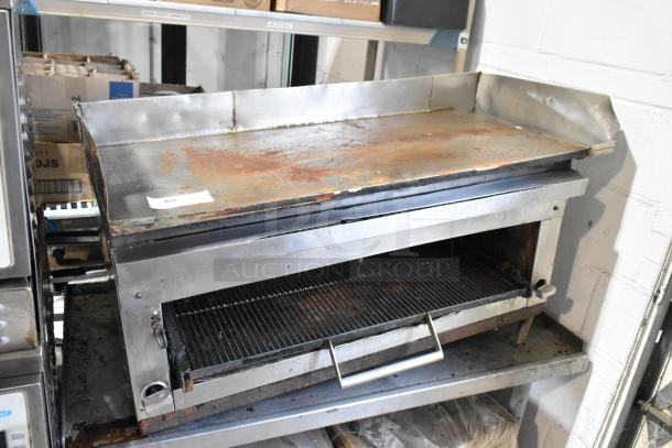 Stainless steel commercial gas flat top griddle with built-in cheese melter on a stand, showing signs of wear.