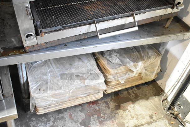 Stainless steel commercial gas griddle with cheese melter on equipment stand, showing signs of use, stored trays beneath.