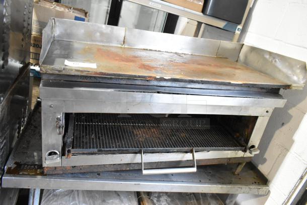 Stainless steel commercial gas flat top griddle with cheese melter on stand, showing signs of wear, suitable for kitchen use.
