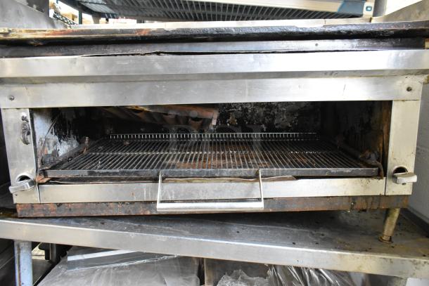Stainless steel gas griddle with cheese melter, rests on equipment stand. Features a flat top surface, used condition.