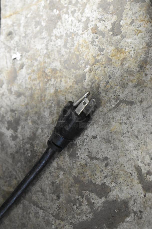Black power plug for Vollrath COA 7002 convection oven on a textured surface, showing a three-prong connection.