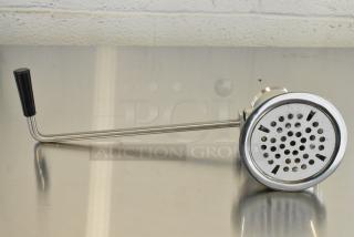 Stainless steel drain with long metal handle, brand new, with scratches and dents visible on surface.