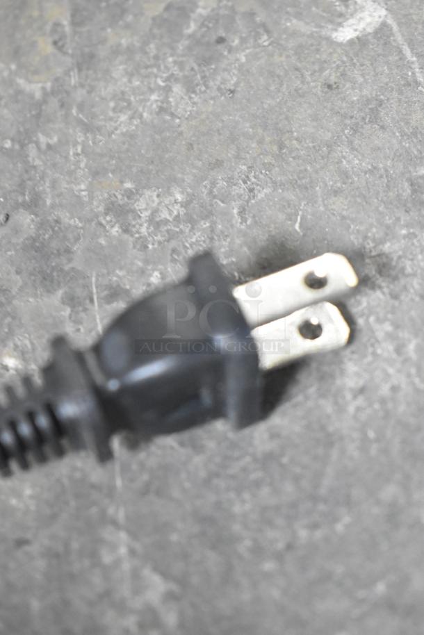Close-up of a black electrical plug for a Proctor Silex 43672PS coffee maker on a gray surface.