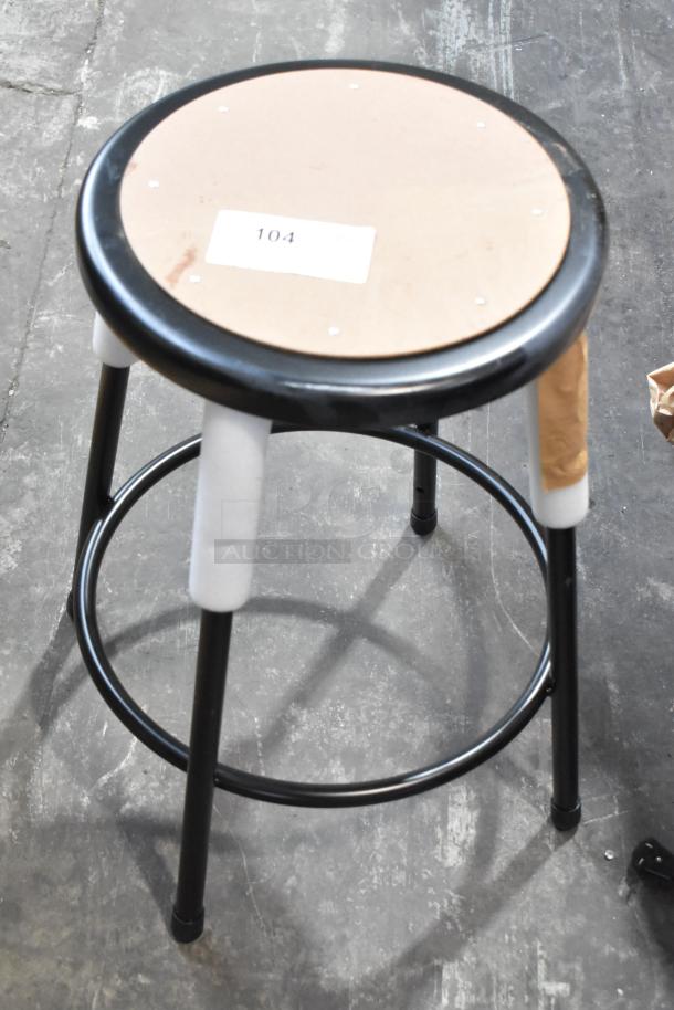 Black metal stool with a round seat. Listed as new with scratch and dent imperfections. Label marked "104" on seat.