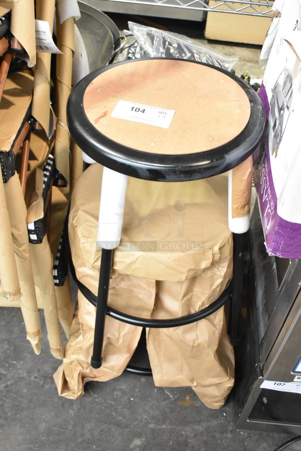 Stack of three black metal stools, brand new condition, with visible scratch and dent marks. Tag indicates "104, QTY 3."