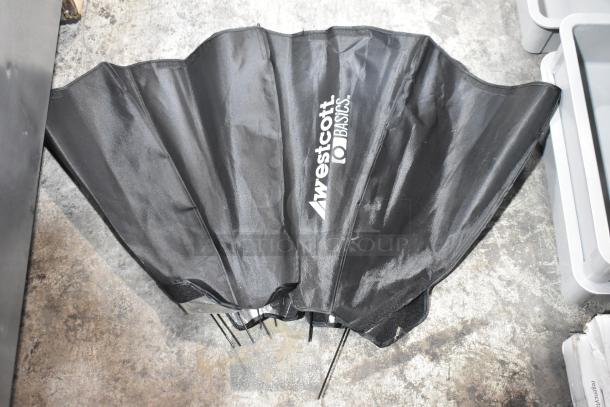 Westcott Basics black umbrella, partially folded, with visible branding, in good condition on a concrete floor.