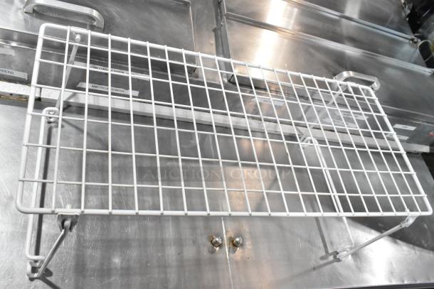 White wire rack shelf on stainless steel surface; part of an auction lot. Features sturdy construction suitable for storage.