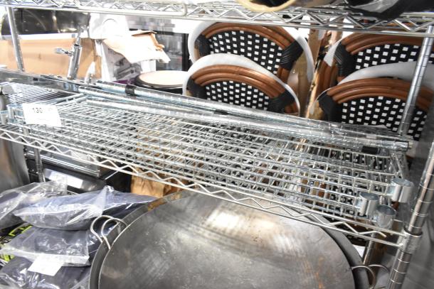 Metal wire shelves and poles on an auction shelf. Includes shelving units, poles, and connectors. Good condition. Tag reads "130".
