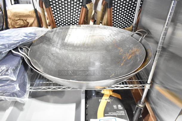 Two brand new metal woks with handles, showing visible scratches and rust marks. Sold as scratch and dent items.