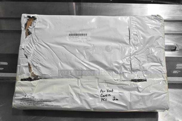 Packaged air vent covers in plastic wrap with visible damage. Handwritten label says "Air Vent Covers PCI 2 ea."