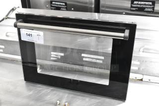 Brand new metal oven door, scratch and dent condition, black frame with stainless steel handle, auction tag visible.