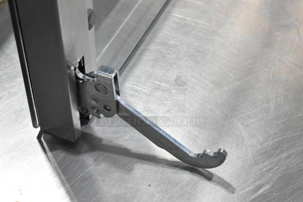 Brand new metal oven door with hinge detail, showing minor scratches and dents.