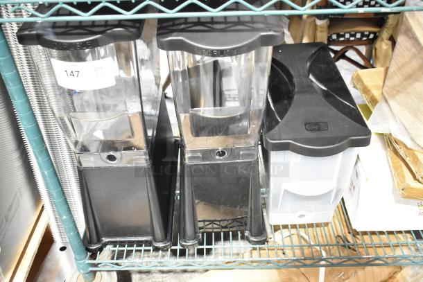 3 brand new Choice 3-gallon black slim beverage dispensers, scratch and dent, clear label 147, on metal shelf.