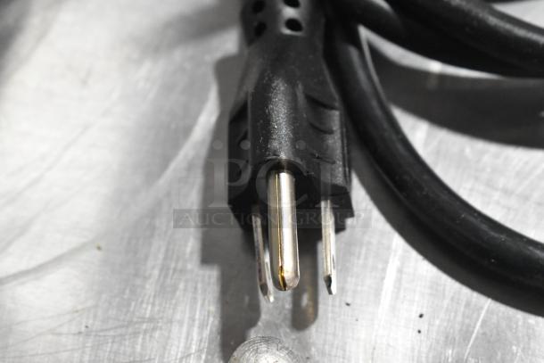 Close-up of a power plug for the Robot Coupe R2UB food processor. Black with three metal prongs.