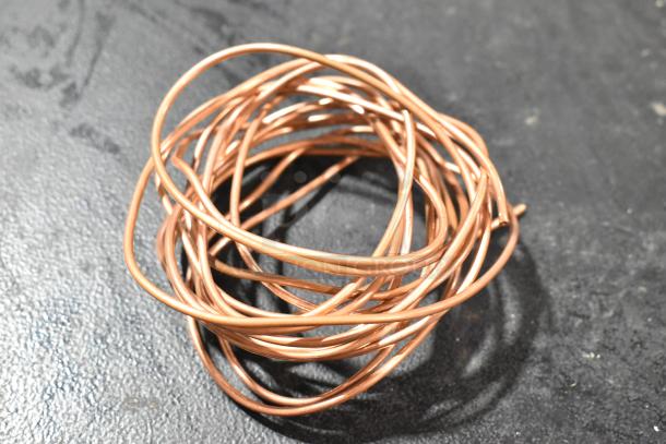 Coiled copper-colored wire on a dark background, part of a new Avantco filter drier auction lot.