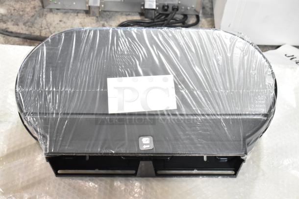 Black poly wall mount toilet paper dispenser, brand new, wrapped in plastic. Some minor scratches and dents visible.