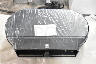 Black poly wall mount toilet paper dispenser, brand new, wrapped in plastic. Some minor scratches and dents visible.