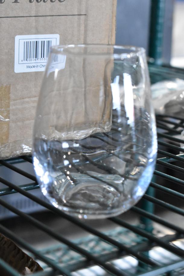 Acopa 12 oz. customizable stemless wine glass, brand new, clear glass, sitting on a shelf near cardboard packaging.