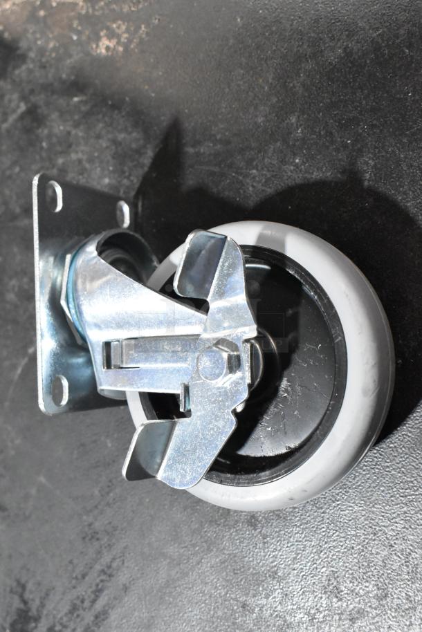 Lot of 4 brand new commercial casters, featuring metal swivel and brake mechanism, with minor scratches and dents visible.