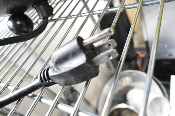 Power plug of Thunder Group SEJ30000C Metal Soup Kettle Food Warmer, 120 Volts, 1 Phase, shown on a metal rack.