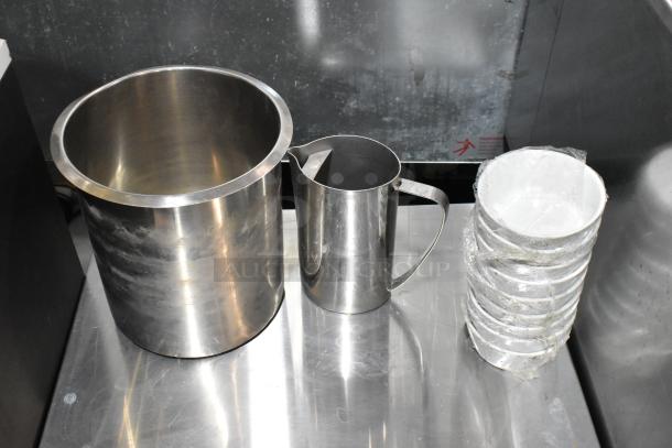 Stainless steel ice bucket and pitcher, stack of plastic cups in protective wrap; items show minimal wear.