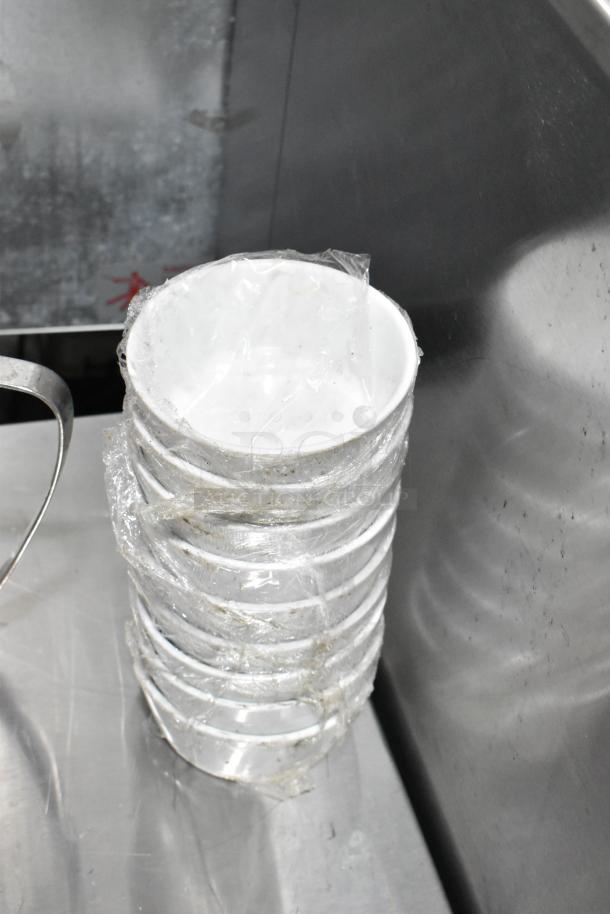 Stack of white plastic bowls wrapped in plastic, slight wear visible, alongside part of a metal handle, possibly from an ice bucket.