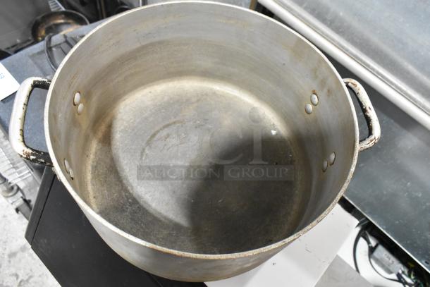 Five used metal stock pots with handles, showing signs of wear. Durable for cooking and storage.