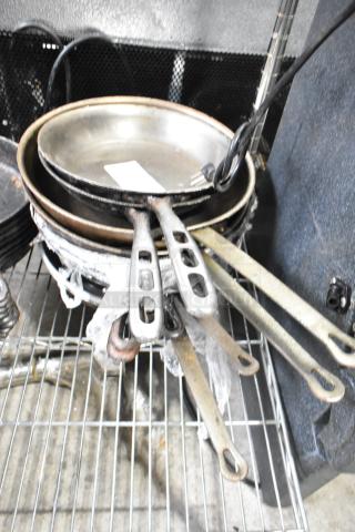Nine assorted pots, including skillets and saucepans, stacked on a metal rack. Visible wear on handles and surfaces.