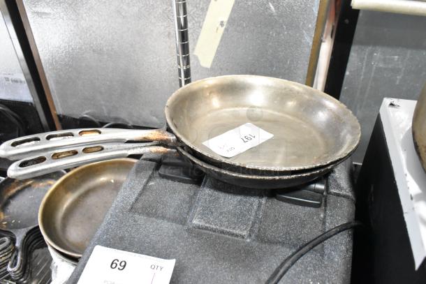 Stack of various skillets and sauce pans with visible wear. Auction tag marked 197 on top skillet.