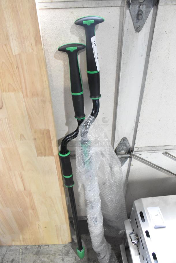Two Unger walking sticks, black with green accents, ergonomic handles, new condition, one partially wrapped, brand visible.