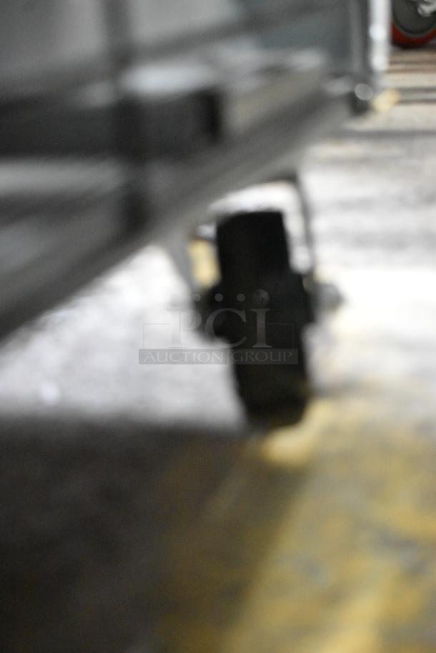 Blurry close-up of a commercial caster on an Accucold AFG26MLLH cooler, showing part of the wheel and floor surface.