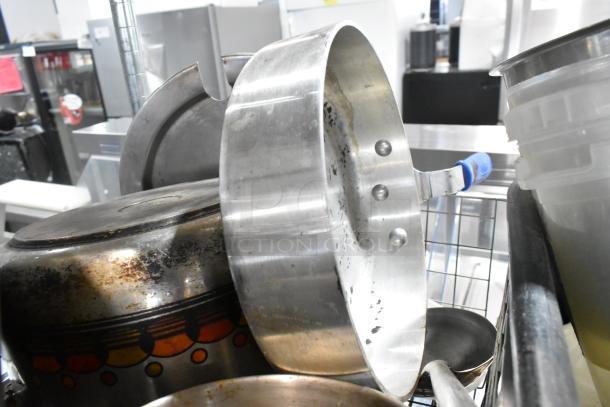 Assorted kitchen items including sauce pans, a poly bus bin, and dishes in varied condition on a metal rack.