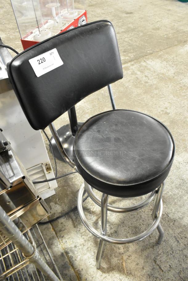 Black stool with backrest on metal frame, showing signs of use. Auction tag "220, Qty 1" attached.