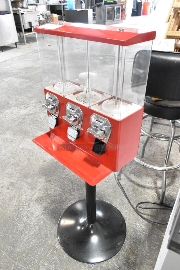 Red metal 3 compartment vending machine on black stand, coin slots, clear containers, good condition.