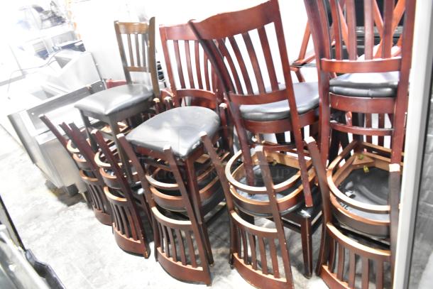 14 wooden dining chairs with black seat cushions stacked. Slatted back design, good condition. Auction: 14 times your bid.