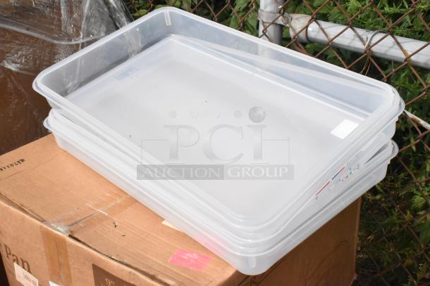 Stack of clear plastic trays atop a cardboard box outside, near chain-link fence. Trays are new and unmarked.