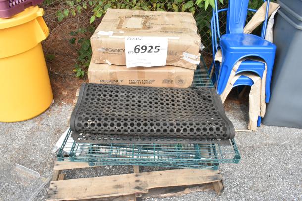 Boxes of Regency 600FT1824SS floor troughs and a black grate on a pallet, with blue chairs in the background.