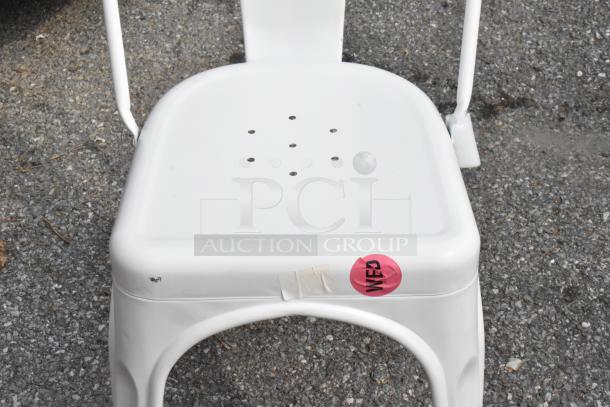 White metal chair with perforated seat, showing minor scratches. Pink sticker marked "WED." Suitable for outdoor use.
