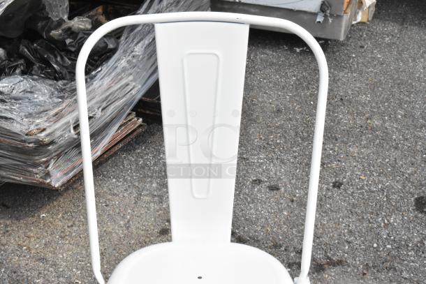 White chair backrest with curved metal frame on outdoor pavement, part of a scratch and dent auction lot.