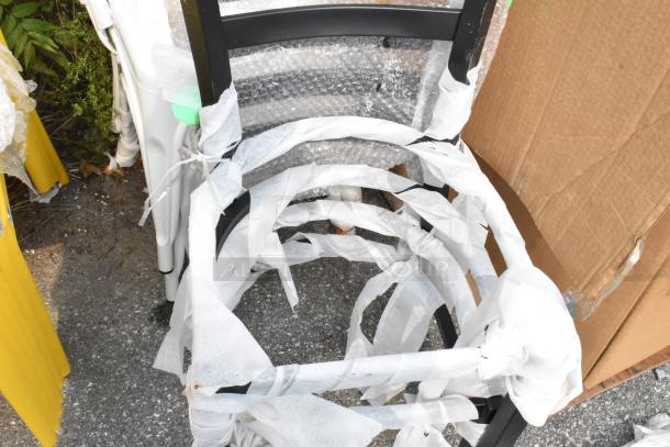 Black metal ladder-back chair frames wrapped in protective material, new condition, bundled for auction.