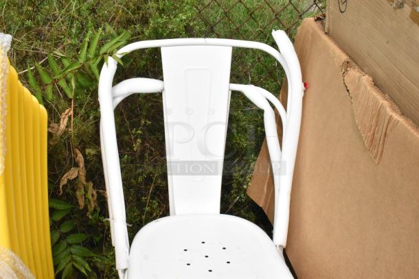 White Tolix-style chair with minor scratches, metal frame, perforated seat, set against a cardboard and greenery backdrop.